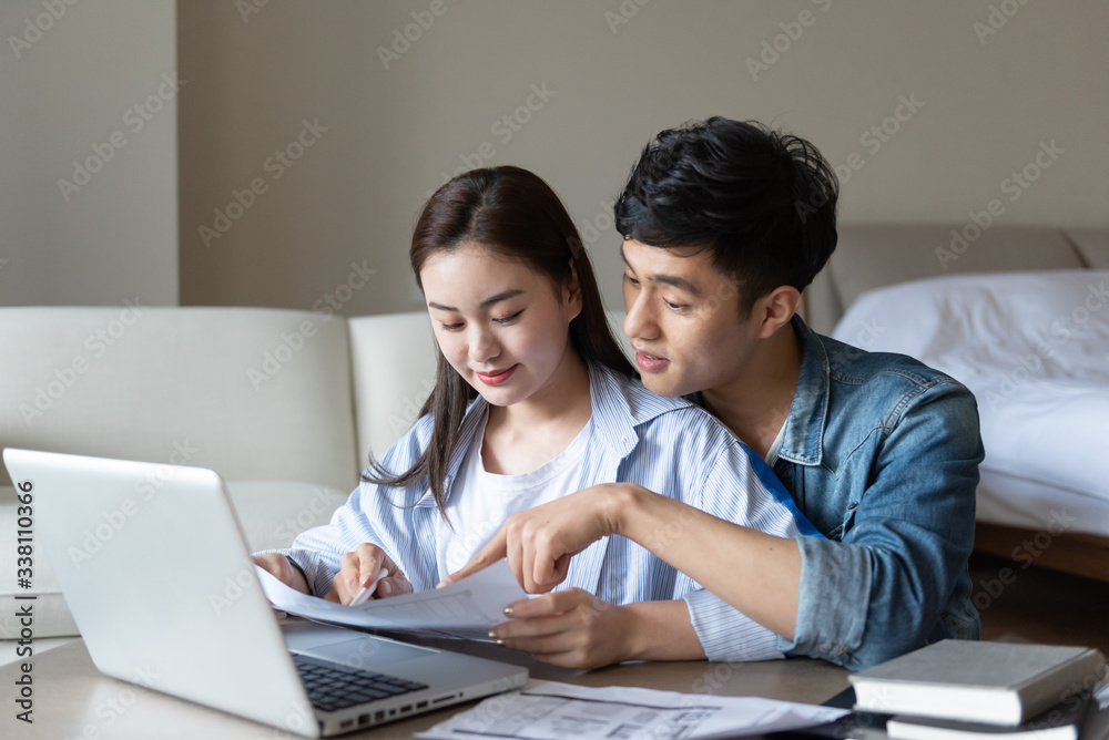 A young asian couple is sitting on a carpet using a computer A young asian couple is sitting on a carpet using a computer