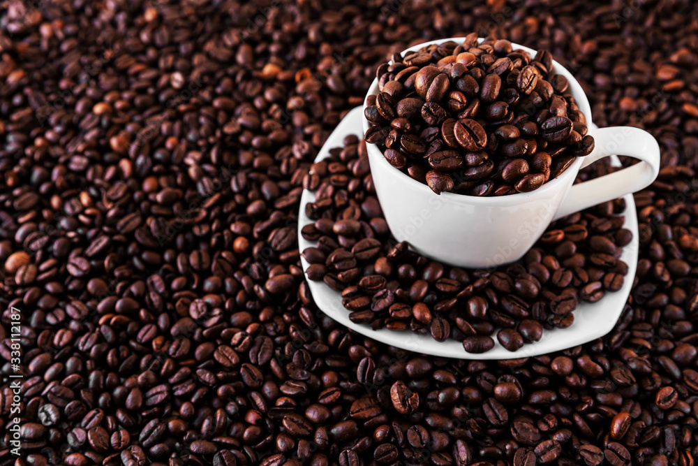 Fototapeta premium White mug and saucer next to roasted coffee beans everywhere, inside the mug and a lot around it. Great for going to a cafe, restaurant, cafeteria menu or as a sign