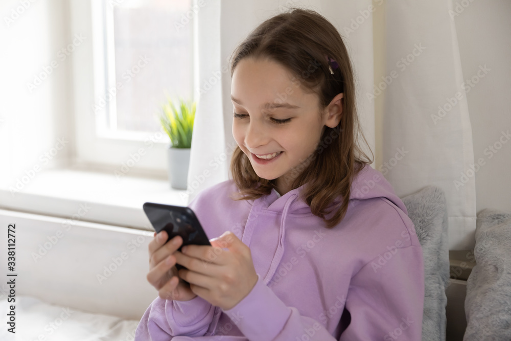 Smiling teen girl using mobile phone apps at home. Happy schoolgirl holding smartphone texting message, chatting with friends in social media, playing game or watching stories looking at cellphone. Smiling teen girl using mobile phone apps at home. Happy schoolgirl holding smartphone texting message, chatting with friends in social media, playing game or watching stories looking at cellphone.