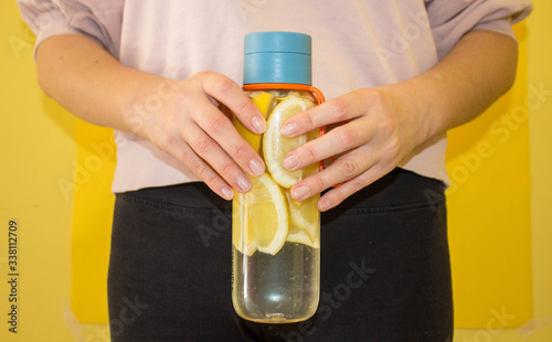 flat lay style concept of healthy lifestyle, sport and fitness at home.  Hand holding bottle of water with lemons on yellow background. Top view.