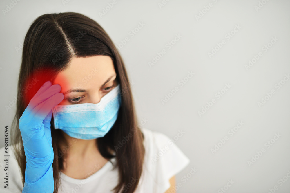 Young woman wearing medical mask, holding her head with her hand, has put on latex gloves.