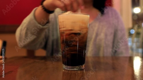 Video of Fresh made Thai tea being mixed by a pretty hand in a clear glass with a clear straw on a wooded table photo