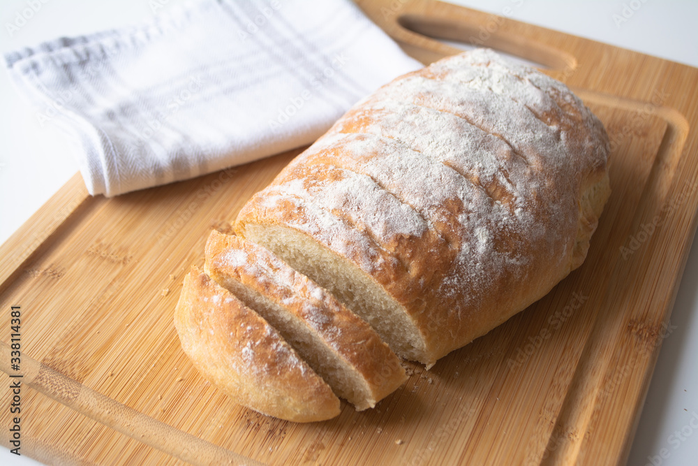 A loaf of homemade fresh bread with flour sprinkled on top in a kitchen towel on wooden cutting board with slices