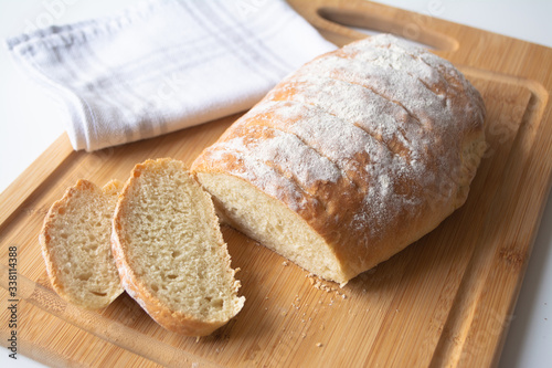 A loaf of homemade fresh bread with flour sprinkled on top in a kitchen towel on wooden cutting board with slices