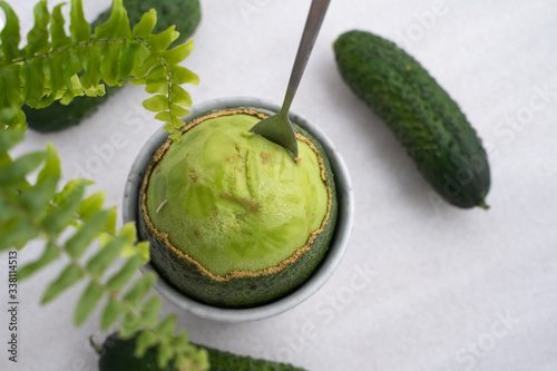 The spoon try to scoop the avocado out of the shell, green food, cucumber background.