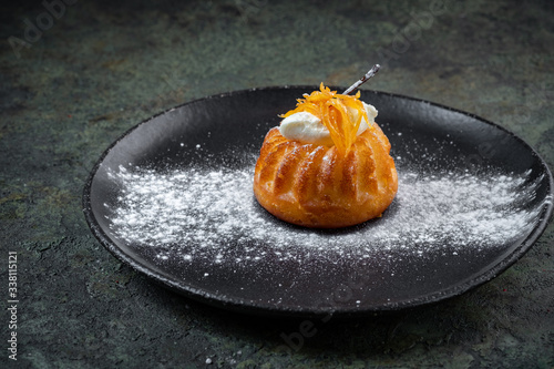 Biscuit dessert rum baba decorated with whipped cream and orange in black plate photo