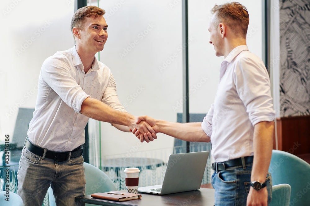 Obraz premium Excited smiling young entrepreneur shaking hand of business partner he is meeting in cafe