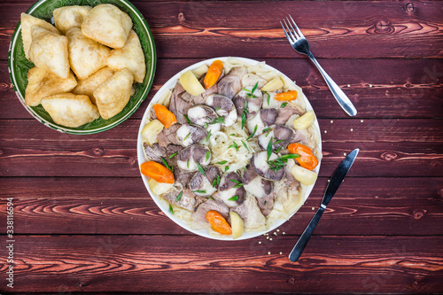 Beshbarmak dish with baursak - traditional Kazakh Asia food and national bread. Noodles with lamb and onion close-up on a plate on the table. Horizontal top view photo