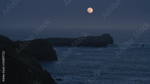 A super-moon over the ocean with cliffs in the foreground.