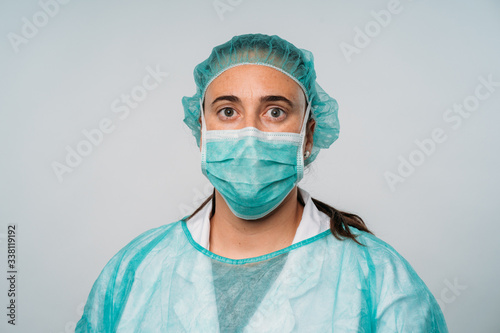 Young female doctor or nurse at camera wearing surgical mask and scrubs on white background