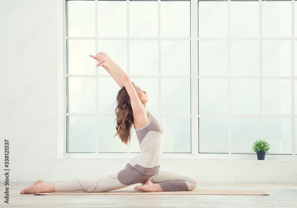 Fototapeta premium Pilates woman. Woman doing yoga exercises on mat in gym. Woman in the window background. Space for text. Woman exercising fitness in gym near the window.