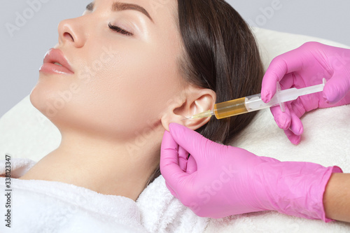 The doctor cosmetologist makes the injections procedure for smoothing wrinkles and against flabbiness of the skin on earlobe of a beautiful, young woman.Women's cosmetology in the beauty salon.