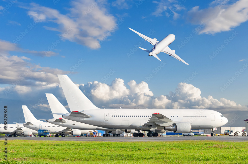 View of the standing planes at the airport and airplane taking off in the sky.