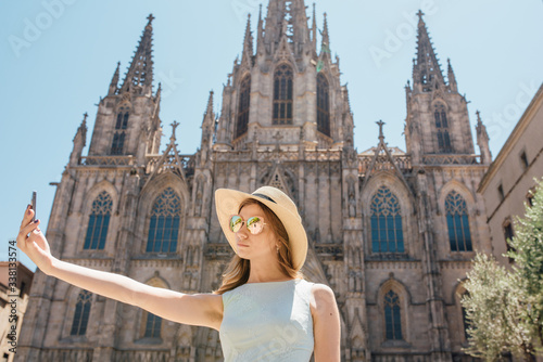 Young and happy tourist woman making selfie photo in front of cathedral in Barcelona