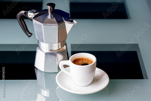 A geyser coffee maker and a Cup of coffee stand on a glass table. Selective focus.