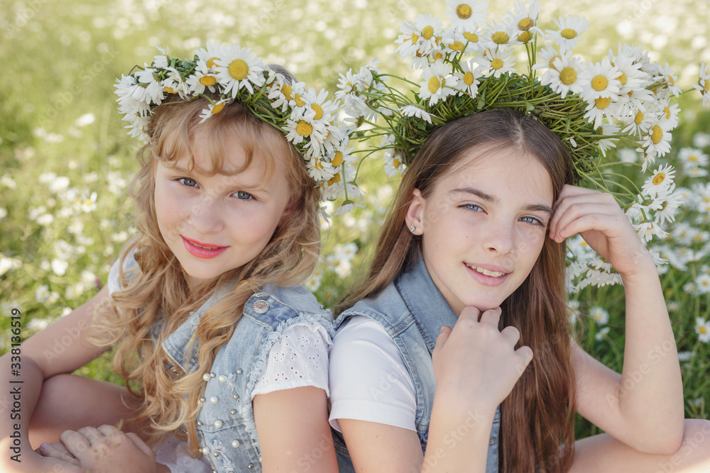 two cute teen girls in denim overalls walk in a daisy field two cute teen girls in denim overalls walk in a daisy field