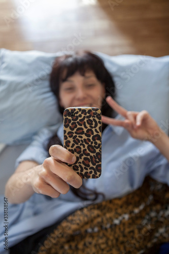 A young woman just woke up from a nap and using her mobile phone. Aerial view of woman lying in bed with matching leopard sheets and mobile. Just awakened.