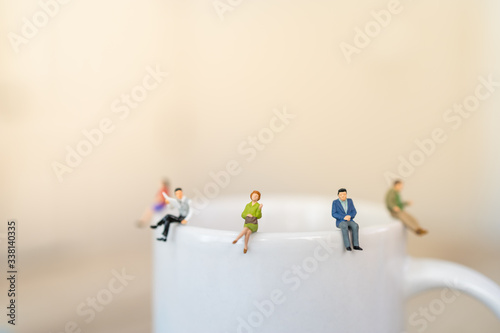 Business, Social Distancing concept for coronavirus 2019 disease (COVID-19) situation . Group of businessman and woman miniature sitting on white mug of hot coffee with copy space.