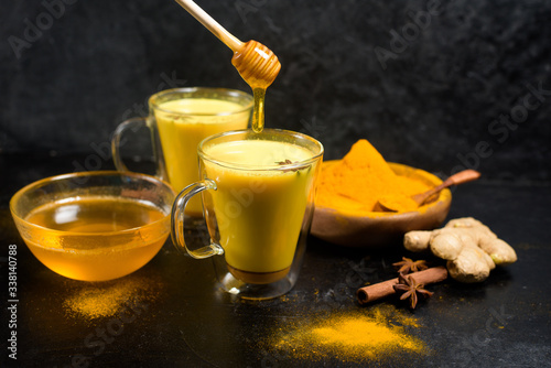Indian traditional Golden milk with turmeric, ginger, spices, honey. healing effect of the drink. ingredients for a Golden drink on a dark background. antiviral therapeutic antioxidant