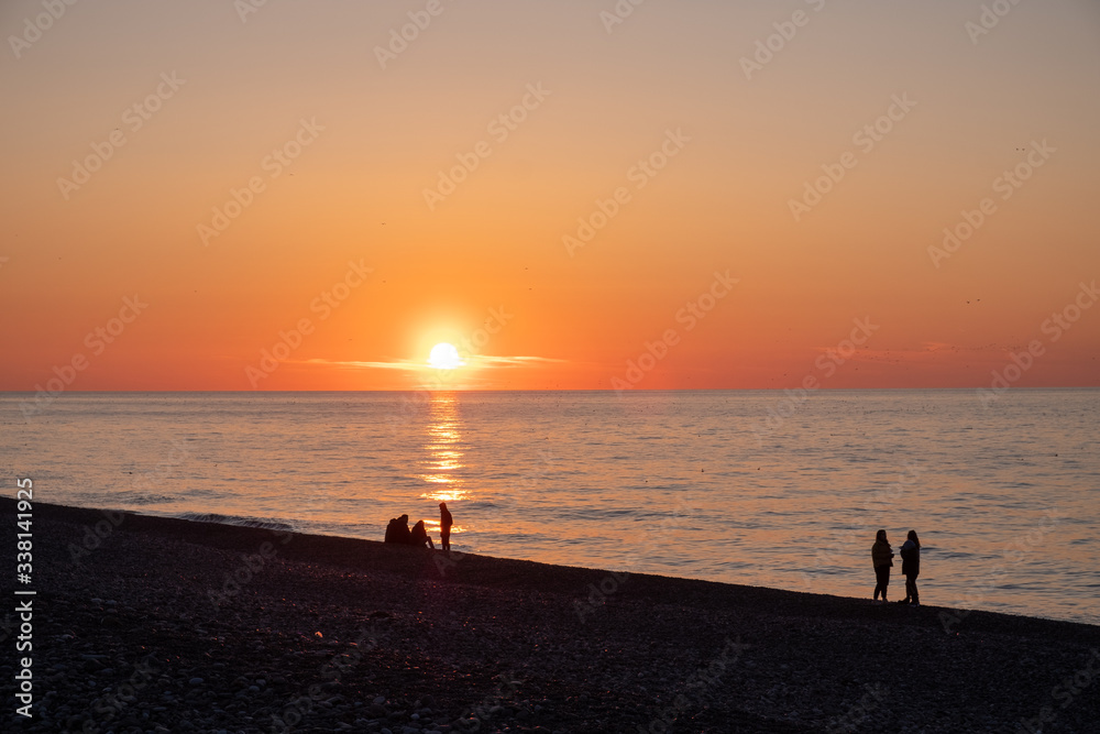 Sunset on the black sea. People walk along the beach and pier. Quiet, calm evening.