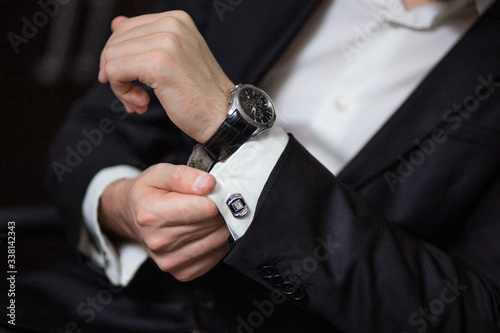 a man's hand with a watch. A man in a black suit adjusts his sleeve. Businessman with a watch on his hand and in a suit
