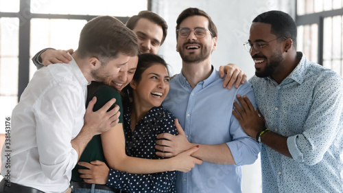 Overjoyed multiracial colleagues have fun laugh celebrate shared win or victory at workplace, happy diverse multiethnic coworkers hug show unity and support at work, teamwork, cooperation concept © fizkes