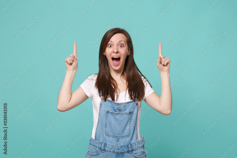 Shocked young brunette woman girl in casual denim clothes posing isolated on blue turquoise wall background. People lifestyle concept. Mock up copy space. Pointing index fingers up keeping mouth open. Shocked young brunette woman girl in casual denim clothes posing isolated on blue turquoise wall background. People lifestyle concept. Mock up copy space. Pointing index fingers up keeping mouth open.