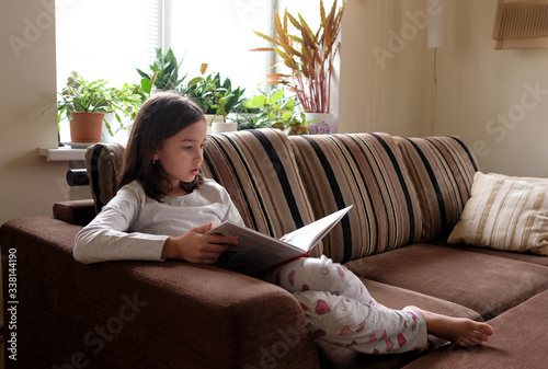 Girl is reading a book on the couch. Distance learning
