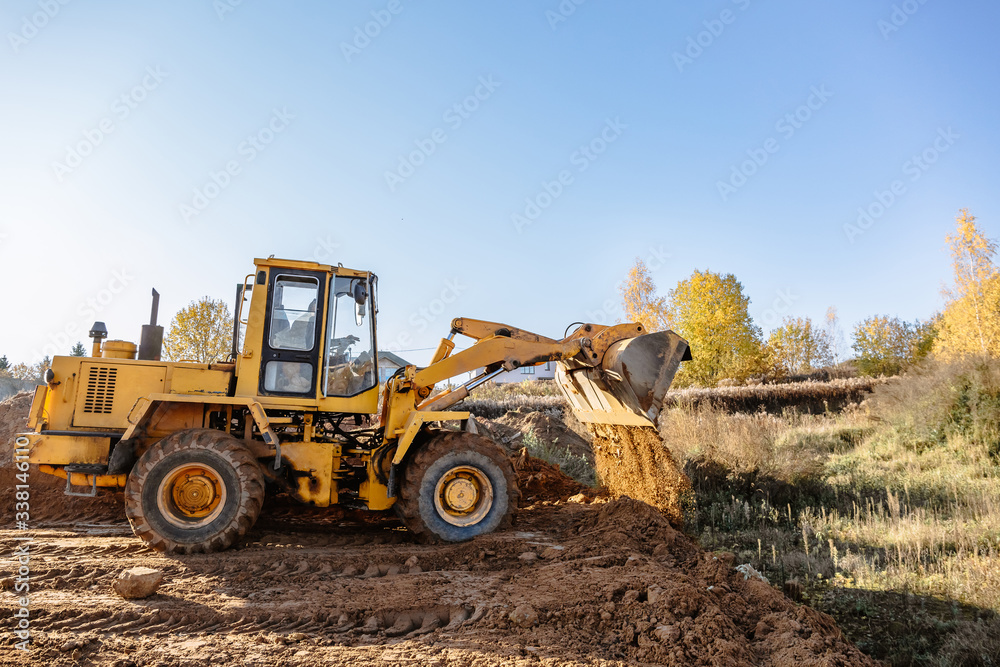 large yellow wheel loader aligns a piece of land for a new building. Preparation of the land for the auction. Leveling the landscape and adding sand for construction.