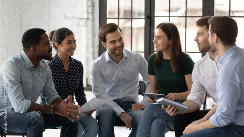 Happy multiracial young people sit in circle in office have fun discussing business ideas together, smiling diverse multiethnic colleagues engaged in teambuilding activity, teamwork concept photo