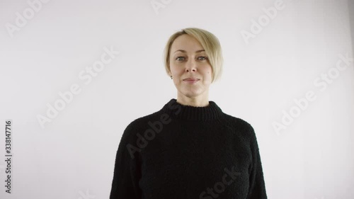 Adult middle aged caucasian blond short haired woman is making a hush gesture to the camera with her index finger against white background in bright interior