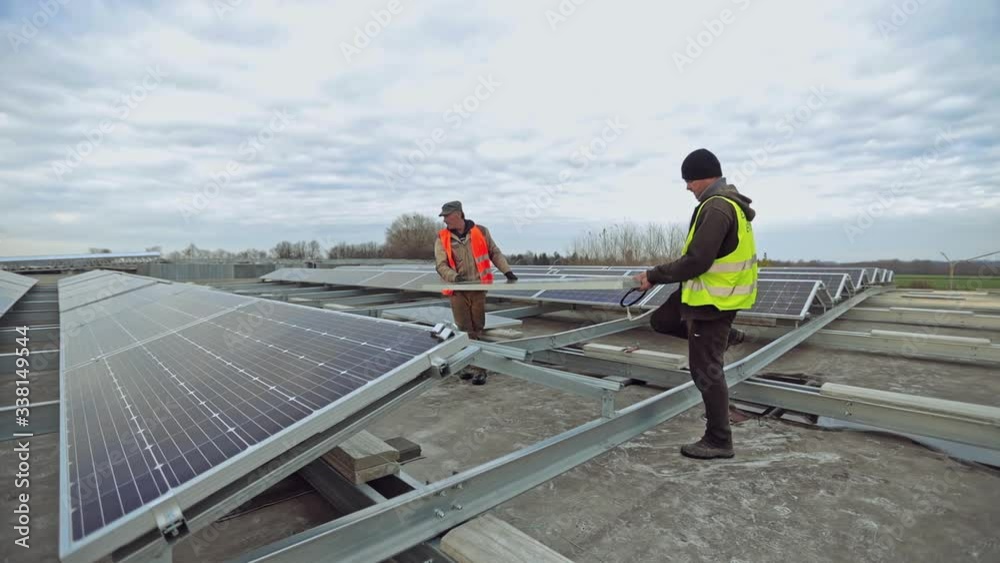 Engineers installing new solar panel. Workers in protective uniform put sunny battery on the metal basis in the solar farm. Alternative source of energy. Engineers installing new solar panel. Workers in protective uniform put sunny battery on the metal basis in the solar farm. Alternative source of energy.