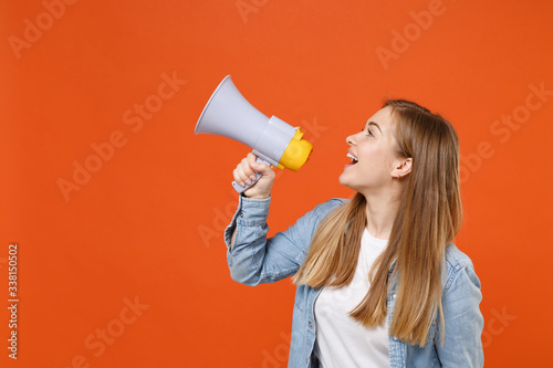 Side view of cheerful young woman girl in casual denim clothes posing isolated on orange background studio portrait. People sincere emotions lifestyle concept. Mock up copy space. Scream in megaphone.