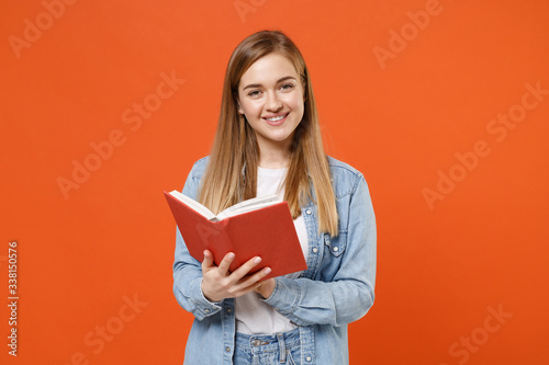 Smiling pretty young woman girl in casual denim clothes posing isolated on bright orange wall background studio portrait. People sincere emotions lifestyle concept. Mock up copy space. Reading book.