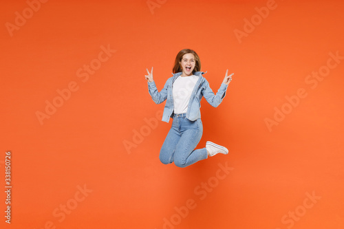 Cheerful young woman girl in casual denim clothes posing isolated on orange background studio portrait. People emotions lifestyle concept. Mock up copy space. Having fun showing victory sign, jumping.