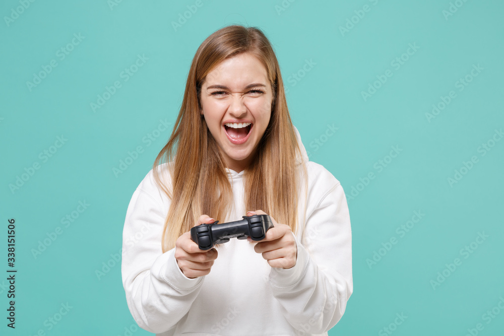Crazy young woman girl in casual white hoodie posing isolated on blue turquoise background studio portrait. People emotions lifestyle concept. Mock up copy space. Play game with joystick, screaming. Crazy young woman girl in casual white hoodie posing isolated on blue turquoise background studio portrait. People emotions lifestyle concept. Mock up copy space. Play game with joystick, screaming.