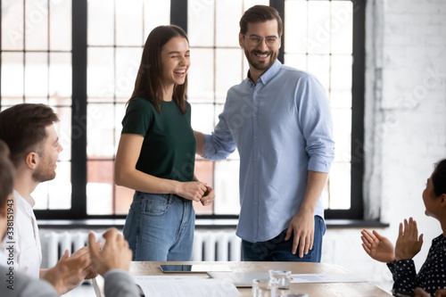 Smiling male employer introduce excited female newcomer to overjoyed diverse coworkers at office briefing, happy businessman welcome new worker at team meeting in boardroom, introduction concept