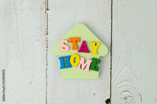Stay home concept with wooden letters and home shape sticky note on wooden background..