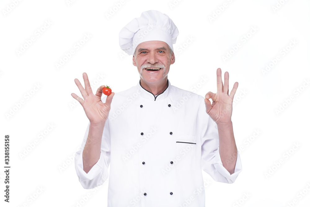 Professional elderly chef in white uniform and hat, holding tomato while staying on white background Professional elderly chef in white uniform and hat, holding tomato while staying on white background