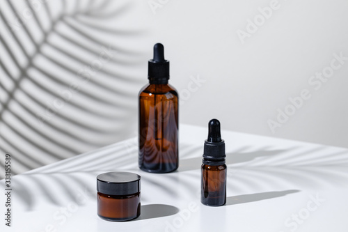 Creative photo of cosmetic bottle with pipette on a white background with shadow of tropical flower. Advertising