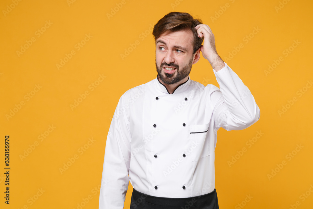 Preoccupied young bearded male chef cook or baker man in white uniform shirt posing isolated on yellow background in studio. Cooking food concept. Mock up copy space. Looking aside, put hand on head. Preoccupied young bearded male chef cook or baker man in white uniform shirt posing isolated on yellow background in studio. Cooking food concept. Mock up copy space. Looking aside, put hand on head.