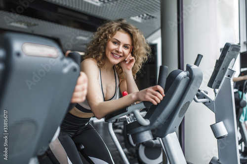 Attractive young woman trainer running on treadmill in gym. Slim girl jogging in fitness club, smiling at camera. Healthy lifestyle concept, cardio training