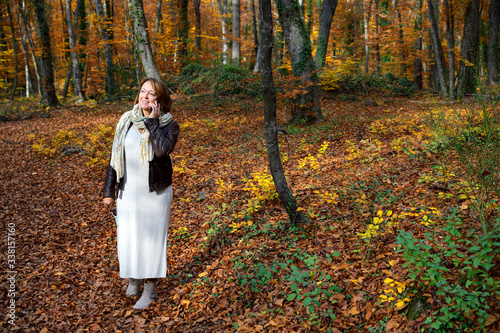 Woman in a beech forest in autumn using her mobile telephone