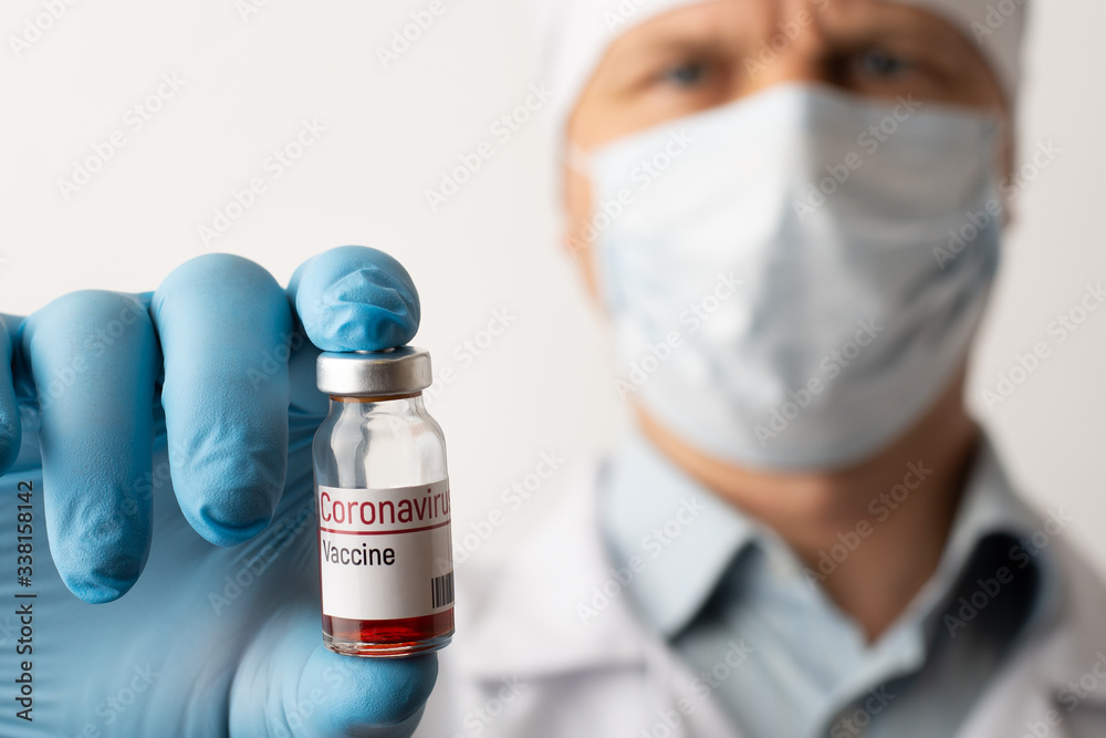 Male doctor in medical glowes and mask holds small bottle with inscription Coronavirus vaccine Male doctor in medical glowes and mask holds small bottle with inscription Coronavirus vaccine
