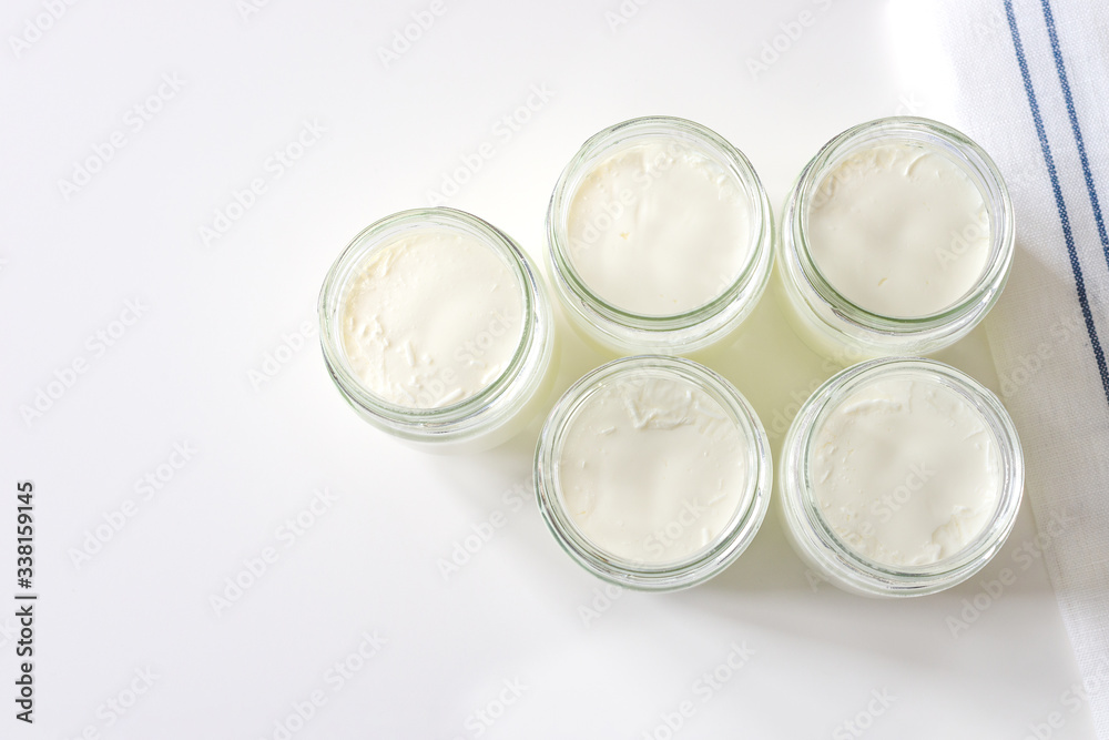 Homemade milk yogurt in glass jars on a white table. Top view, copyspace. Cooking at home during the COVID-19 quarantine
