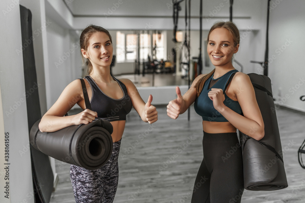 Happy fitness girls, with a yoga mat showing okay signal after team training at modern gym Happy fitness girls, with a yoga mat showing okay signal after team training at modern gym