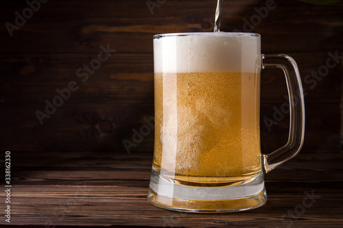 Light beer is poured into a mug on a wooden table. Beer in a mug.