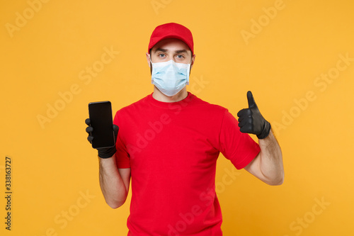 Delivery man in red cap blank t-shirt uniform sterile face mask gloves isolated on yellow background studio Guy courier hold mobile cell phone Service quarantine pandemic coronavirus 2019-ncov concept
