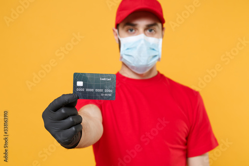 Delivery man red cap blank t-shirt uniform mask gloves isolated on yellow background studio Guy employee work courier hold credit card Service quarantine pandemic coronavirus virus 2019-ncov concept.