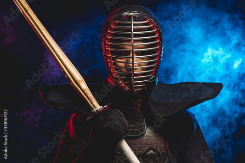 portrait of kendo fighter in uniform and protective helmet. combat warrior holding shinai in hand bamboo sword isolated over smoky space